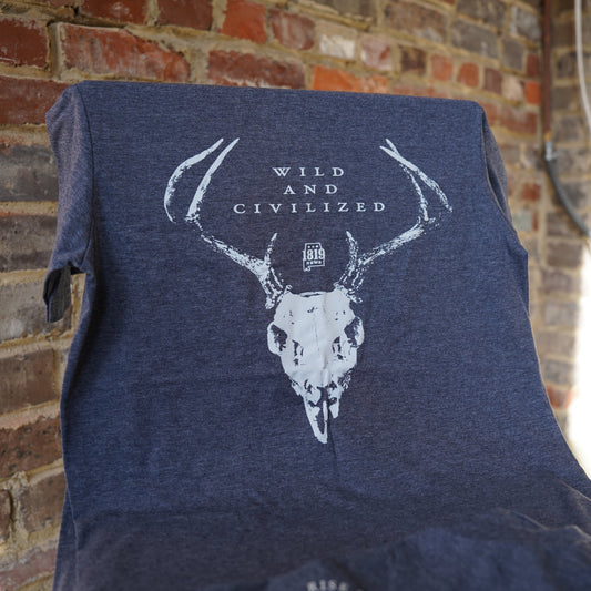 Navy blue t-shirt with white bull skull design and text against a brick wall.