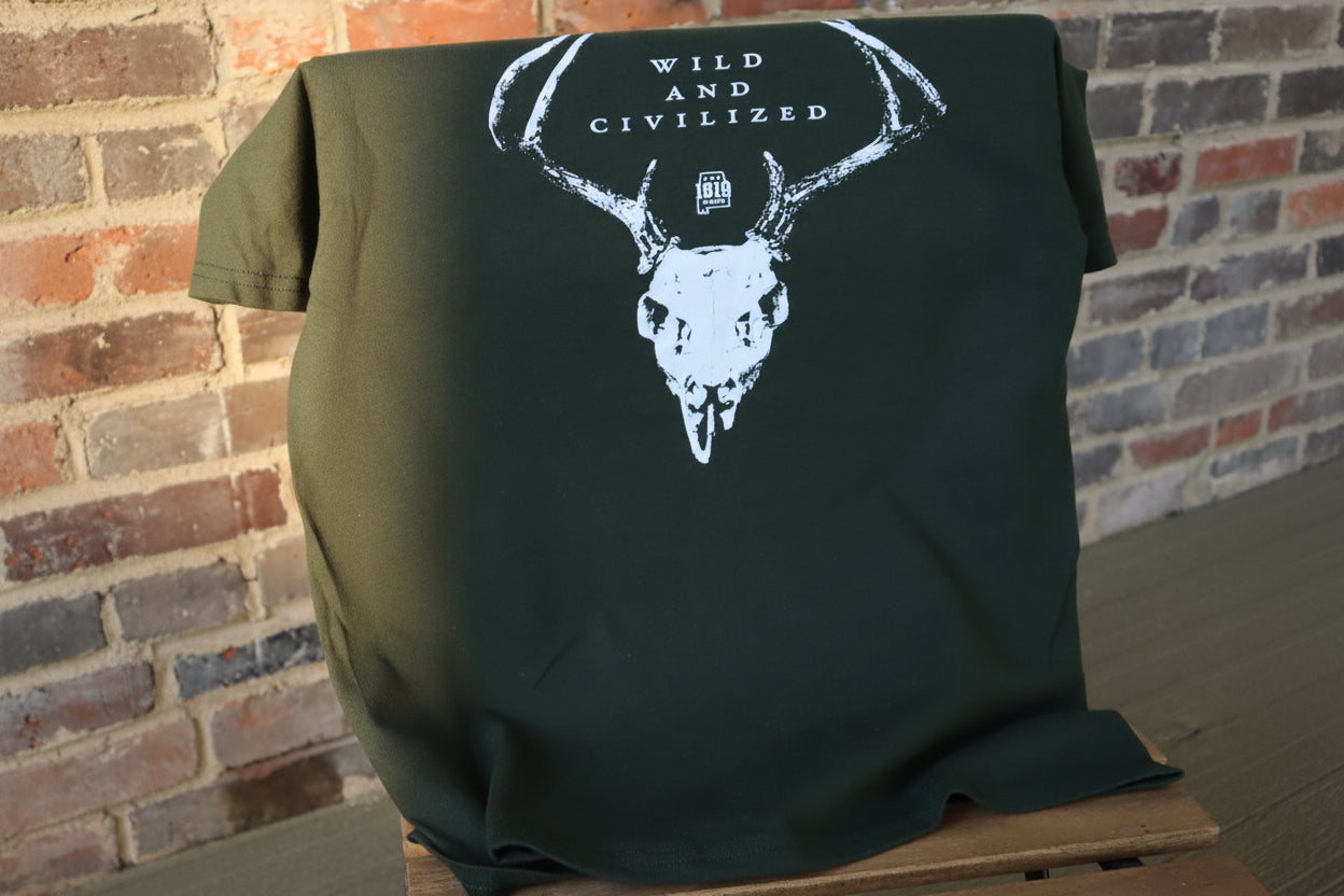 Dark green t-shirt with white graphic design on a wooden pallet against a brick wall.